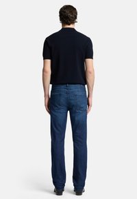 Jeans scuri blu da uomo e una polo nera a maniche corte, visti da dietro. I jeans hanno una vestibilità dritta con due tasche posteriori.