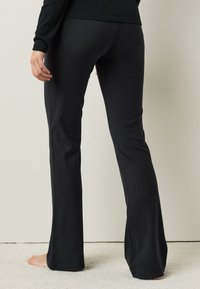 Pantalones negros acampanados hechos de tela suave, con una textura lisa. El diseño es ajustado en la cintura y se desplaza suelto desde la rodilla.