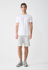 Camiseta blanca de cuello redondo combinada con pantalones cortos de sudadera gris claro con puños enrollados y zapatillas deportivas grises con acentos reflectantes.