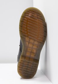 Suela de zapato de goma negra con surcos texturizados y un lado inferior duradero de color marrón amarillento, con logotipo de la marca en relieve y símbolos de cuidado.