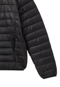 Giacca leggera nera trapuntata con tasca con zip sul lato sinistro, caratterizzata da una texture liscia e lucida e un design delle maniche aderente.