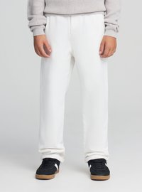 Białe bawełniane spodnie o luźnym kroju, z elastycznym pasem, mankietami u dołu oraz w połączeniu z czarnymi tenisówkami z białymi akcentami.