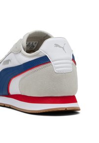 Rückansicht eines weißen und grauen Puma-Sneakers mit einem blauen Streifen, roter Zwischensohle und brauner Außensohle auf einem weißen Hintergrund.