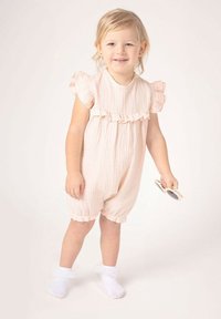 Jasnoróżowy bawełniany kombinezon z falbankami na rękawach i elastycznymi mankietami, wykonany z teksturowanej tkaniny. Dziecko trzyma okulary przeciwsłoneczne, ma na sobie białe skarpetki do kostek.