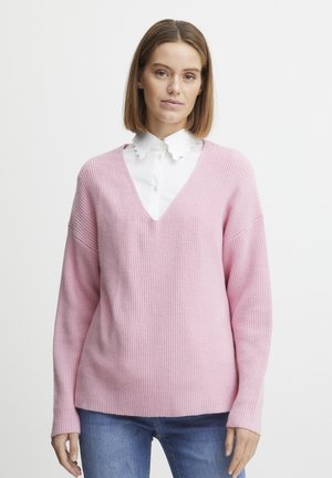 Roze geribde gebreide trui met een V-hals, ontspannen pasvorm en lange mouwen, gecombineerd met een witte blouse met kraag eronder.