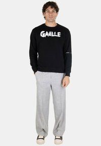 Felpa nera con il testo bianco "GAËLLE", pantaloni a scacchi grigi e sneakers nere e crema. Design semplice, vestibilità moderna e texture morbida.