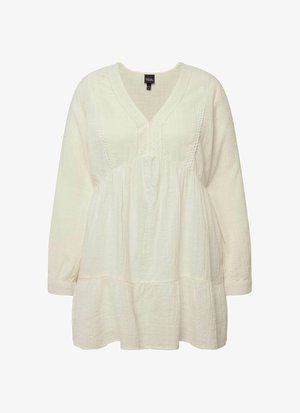 Blusa de algodón blanca y texturizada con escote en V, mangas largas y dobladillo acampanado. Presenta delicadas costuras a lo largo del escote.