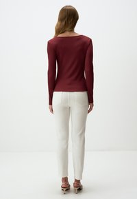 Bordeaux overhemd met lange mouwen en een bootnek, gecombineerd met witte slim-fit broek en beige haksandalen. Glad textiel.