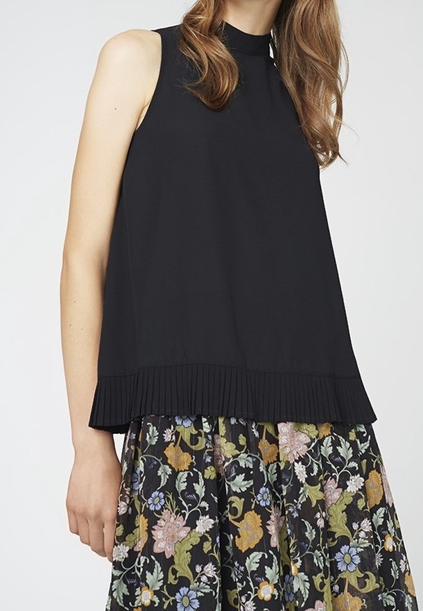 Haut noir sans manches avec ourlet plissé, accompagné d'une jupe à motif floral comprenant des fleurs vertes, jaunes, roses et bleues.