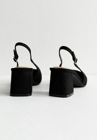 Scarpe slingback in suede nero con tacco largo, cinturino regolabile e soletta morbida. La parte superiore testurizzata aumenta l'interesse visivo.