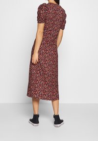 Květinové šaty střední délky s nafouklými rukávy v tmavé vzorované látce. Nositelná s černými vysokými teniskami. Má přiléhavý pas.