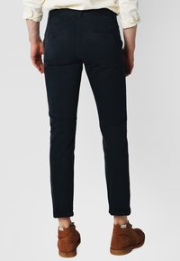 Mørkeblå slim-fit bukser lavet af bomuldsblanding, med baglommer og en glat tekstur. Komplementeret af brune suede sko.
