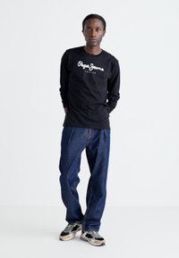 Camisa negra de manga larga con el logo "Pepe Jeans London", combinada con unos vaqueros oscuros de corte holgado y zapatillas multicolores.