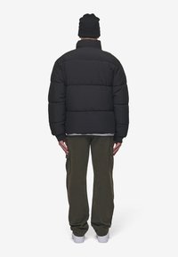 Sort polstret jakke med høj krave, har synlige stikninger og elastiske manchetter. Bær den med olivengrønne cargobukser og hvide sneakers.