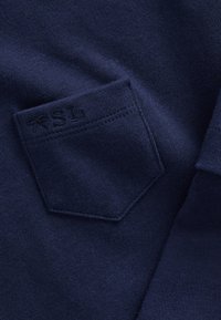 Granatowy materiał o gładkiej fakturze, z małą naszywaną kieszonką z wytłoczonym logo "SL" po lewej stronie.