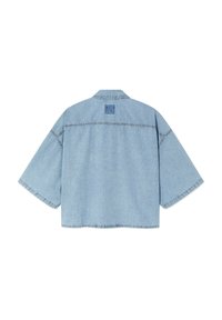 Veste en jean courte bleu clair avec des manches larges et un petit écusson logo "American Vintage" sur le haut du dos.