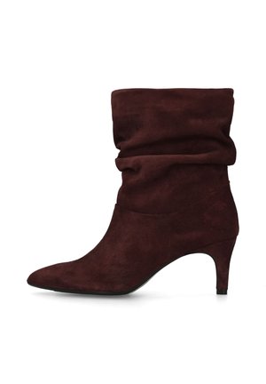 Donkerbruine suède laars tot halverwege de kuit met een slouchy uitstraling, spitse neus en slanke kittenhak, zijaanzicht tegen een witte achtergrond.