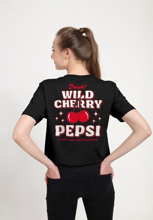 Jonge vrouw met bruin haar in een paardenstaart die een zwart T-shirt draagt met rode kersen en witte tekst met de tekst "Drink! Wild Cherry Pepsi."