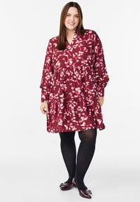 Bordo suknelė su baltais gėlių raštais, ilgomis rankovėmis ir sluoksniuotu sijonu. Dėvima su juodomis pėdkelnėmis ir bordinėmis bateliais, turinčiais dekoratyvų sagtį.