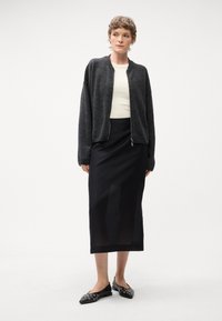 Długa czarna spódnica, dopasowana w talii, zestawiona z szarym swetrem na zamek. Czarne baleriny z srebrnymi akcentami dopełniają stylizację.