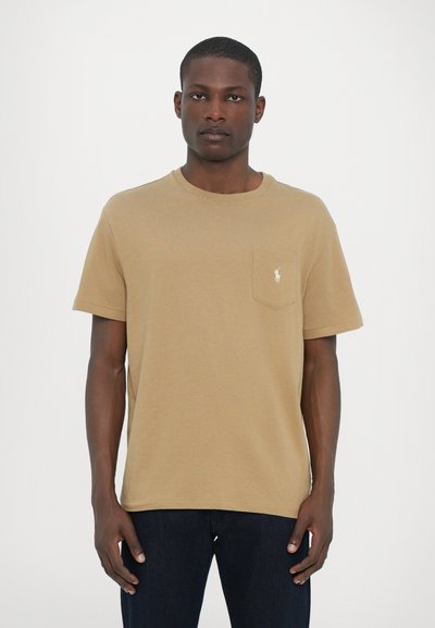 T-shirt en coton beige avec col rond, manches courtes et une poche avec un petit logo brodé sur le côté gauche.