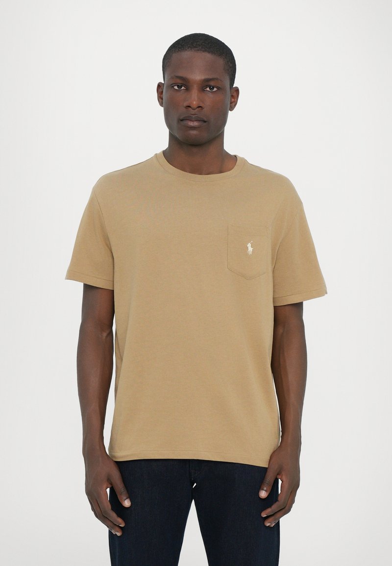 T-shirt en coton beige avec col rond, manches courtes et une poche avec un petit logo brodé sur le côté gauche.