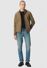 Felpa marrone con cappuccio e tasche frontali abbinata a jeans azzurri e stivali neri. Design semplice, trama morbida e vestibilità casual.