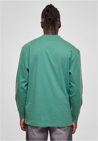 Camiseta de algodón verde de manga larga con cuello redondo y corte relajado, que presenta una textura suave y costuras de hombro caídas.