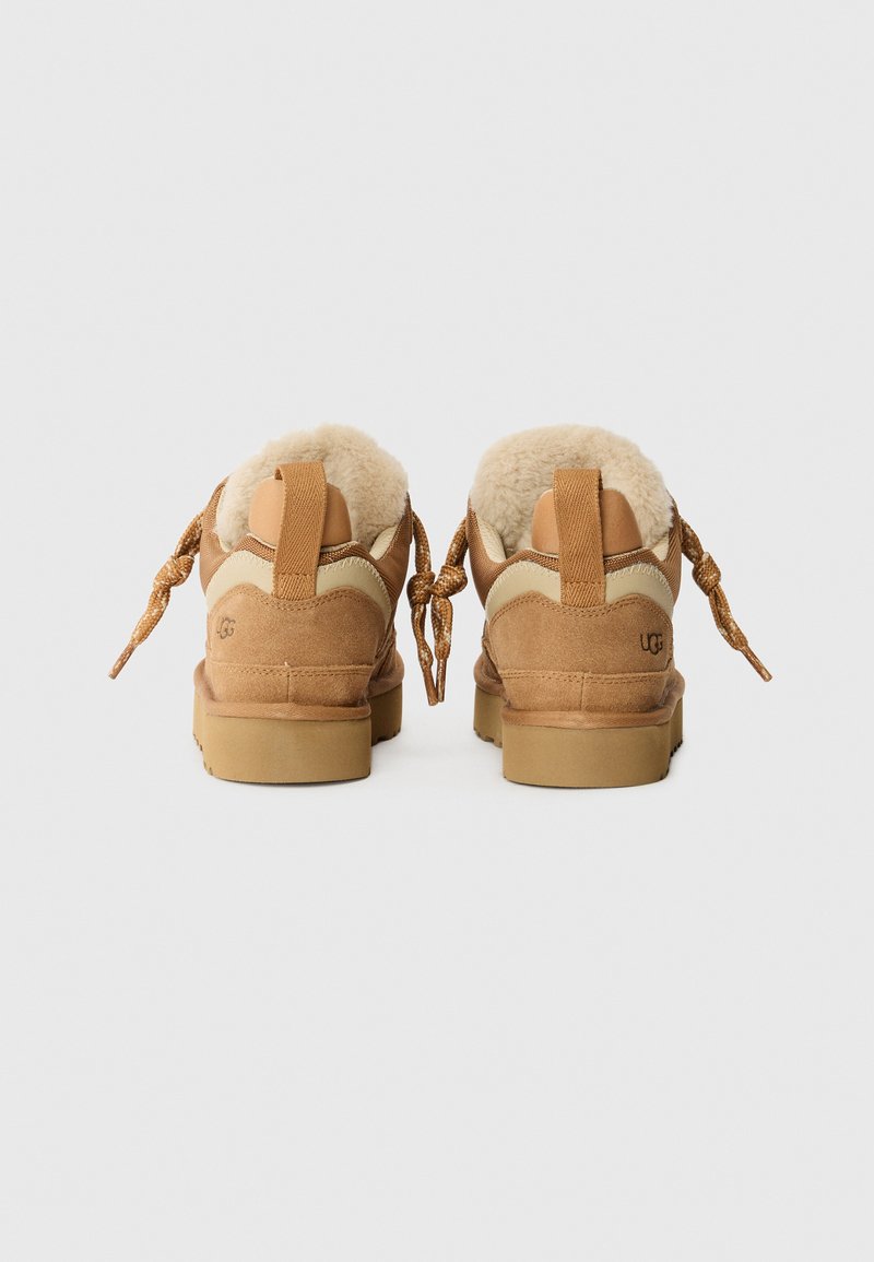 Braune Wildlederschuhe mit cremefarbenen Akzenten, flauschiger Innenauskleidung und dicken beigen Sohlen. Verfügt über geflochtene Schnürsenkel und ein UGG-Logo auf der Ferse.