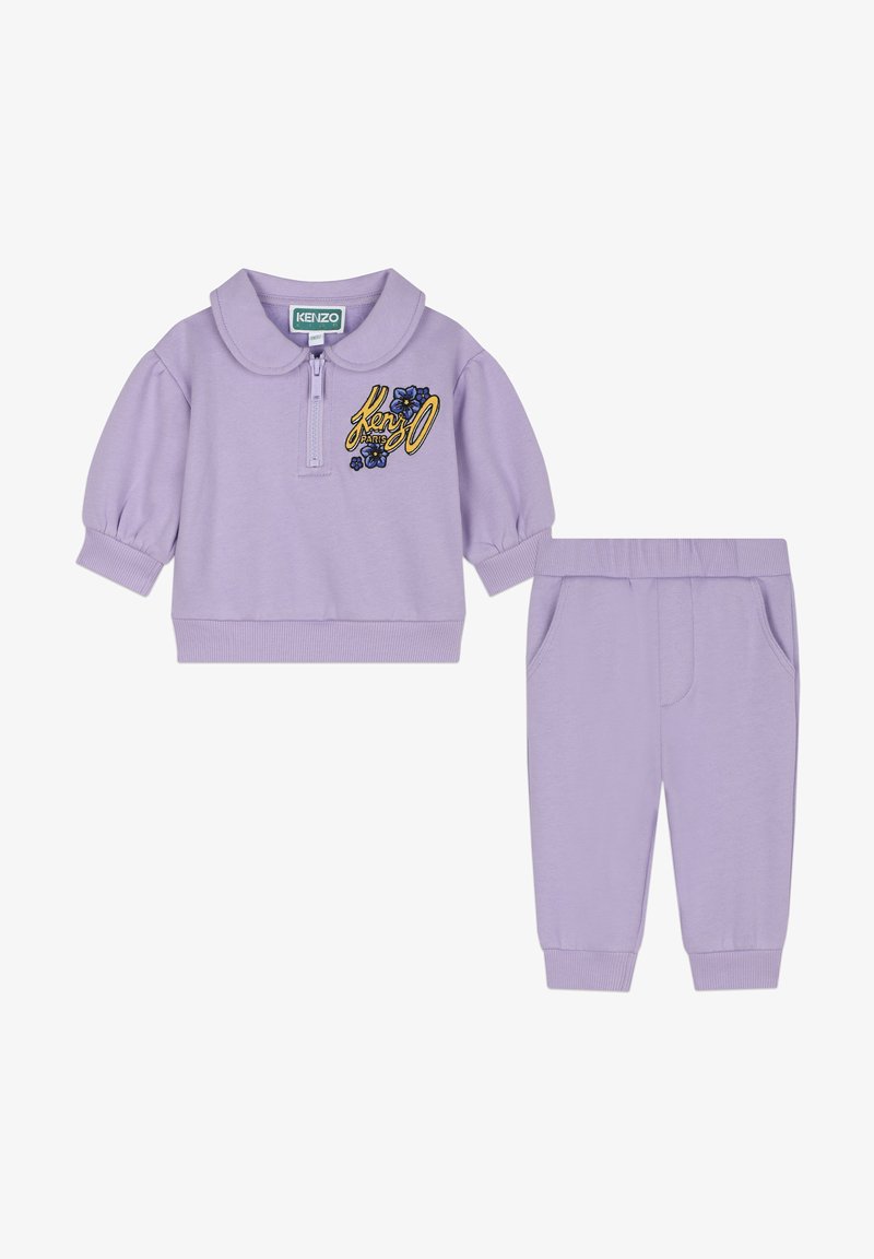 Ensemble deux pièces lilas comprenant un haut zippé avec col, des manches courtes bouffantes, et un pantalon assorti avec poches et poignets côtelés.