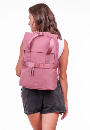 Pink fabric backpack with adjustable shoulder straps, top handle, and front flap. Features logo and decorative straps. Smooth texture.