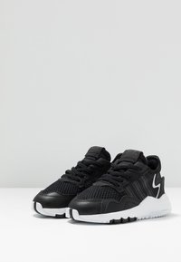 Baskets de sport noires avec une tige en mesh texturé, des accents synthétiques noirs, une semelle en caoutchouc blanche et un détail de marque discret.