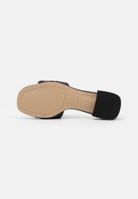 Black heeled sandal featuring a smooth leather upper, beige sole, and textured rubber grip. Adjustable strap for secure fit.