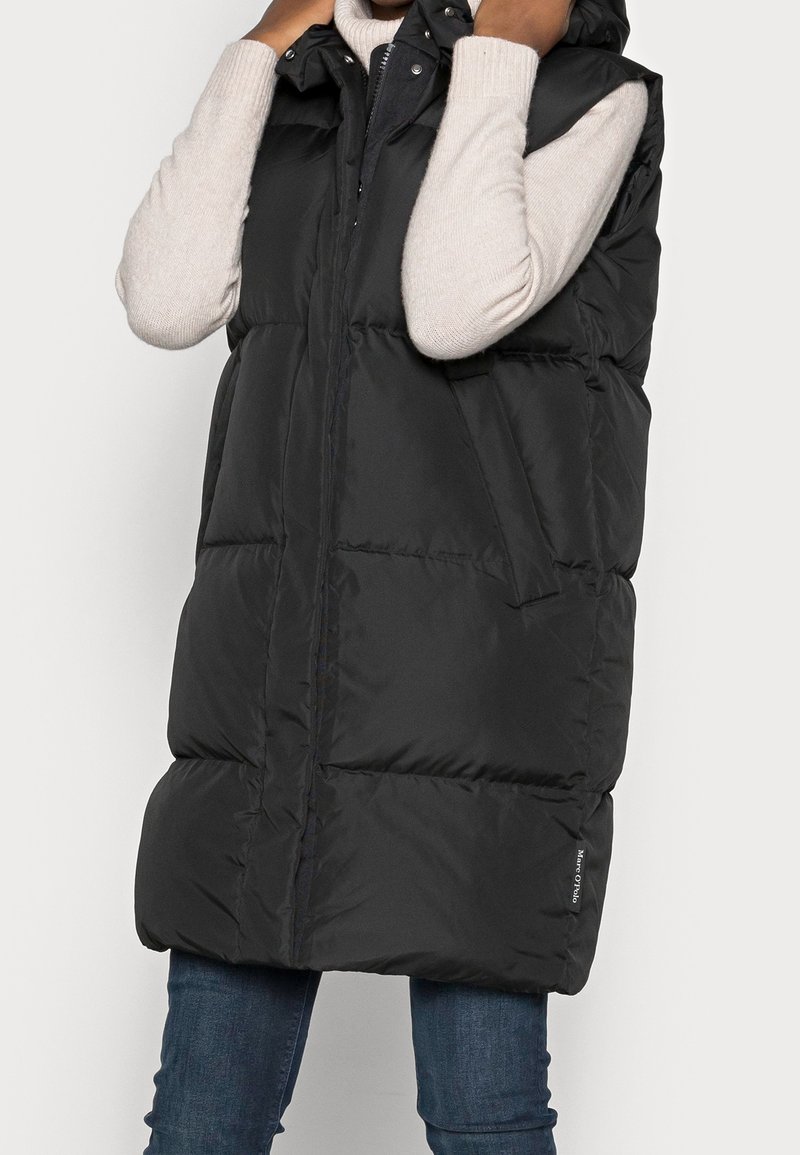 Gilet imbottito nero con cappuccio, caratterizzato da una chiusura con zip sul davanti, tasche laterali e una vestibilità ampia. Realizzato in un materiale liscio e trapuntato.