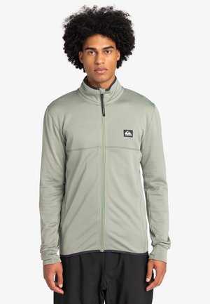 Green zip-up jacket made of textured fabric, featuring a high collar, logo patch on the left chest, and fitted long sleeves.