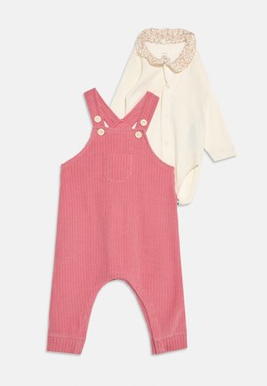 Salopette bébé en velours côtelé rose avec poche avant, associée à un body blanc à manches longues avec col à volants fleuris.