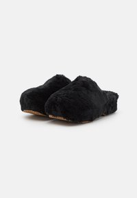 Een paar zwarte, fluffy instap-slippers met bruine gestructureerde zolen, getoond onder een lichte hoek op een witte achtergrond.