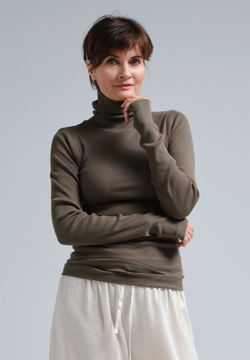 Brauner gerippter Stehkragenpullover aus elastischem Material, mit langen Ärmeln und tailliertem Design, kombiniert mit hellen, lockeren Hosen.