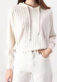 Hoodie w kolorze kremowym, z żeberkowym wzorem, z sznurkami i srebrnymi detalami, w połączeniu z białymi dżinsami z wysokim stanem. Miękka faktura, luźny krój.