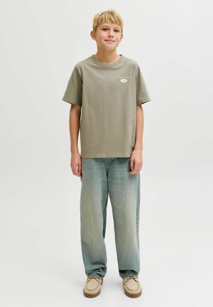 Jasno oliwkowo-zielona koszulka z okrągłym dekoltem i krótkimi rękawami, w połączeniu z luźnymi niebieskimi dżinsami. Prosty fason bez widocznych wzorów.