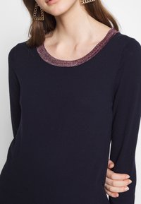 Maglietta a maniche lunghe blu navy con scollatura rotonda, caratterizzata da un bordo testurizzato in rosa scuro. Tessuto morbido, design aderente, eleganza discreta.
