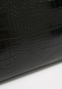 Musta krokotiilikuvioitu nahkalaukku, jossa sileä kiiltävä pinta ja monimutkaiset kuviot, ja jonka muoto on jämäkkä suorakaide.