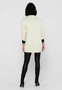 Krämbelagd stickad tröja med långa ärmar och åtsittande nederkant, i kombination med svarta läderleggings och knähöga svarta stövlar.