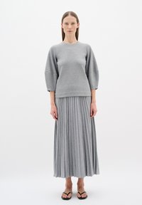 Grauer Pullover mit 3/4-Ärmeln, kombiniert mit einem grauen Maxiröcke mit Falten. Die Texturen sind weich und glatt, ergänzt durch schwarze Flip-Flops.