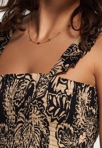 Dress with a black floral pattern on a beige background, featuring a smocked bodice and ruffled shoulder straps. Gold necklace with colored stones.