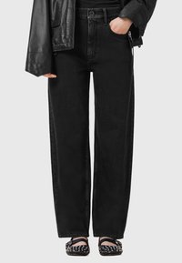 Zwarte high-waisted wijde spijkerbroek gemaakt van denim, met een klassiek vijf-pocket ontwerp en een knoopsluiting, gecombineerd met studsandalen.