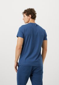 Μπλε κοντομάνικο μπλουζάκι από μαλακό ύφασμα, με στρογγυλή λαιμόκοψη και μια μικρή λεπτομέρεια κουμπιού στο πίσω μέρος. Απαλή υφή.