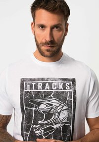 Camiseta de algodón blanca con un gráfico negro de un casco de motocross, con el texto "DIRT TRACKS" encima y un fondo texturizado.