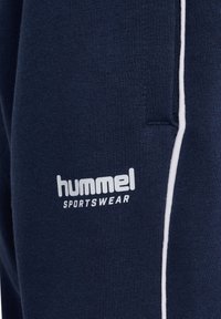 Close-up af mørkeblå hummel sportstøjsstof med hvidt logo og lodret hvid stribe.