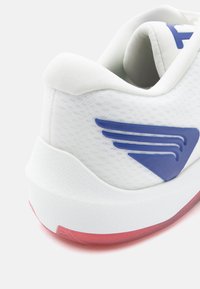 Białe sportowe buty z siateczkową cholewką, niebieskimi akcentami przypominającymi skrzydła i teksturowaną białą podeszwą. Posiadają przezroczystą czerwoną podeszwę zewnętrzną.